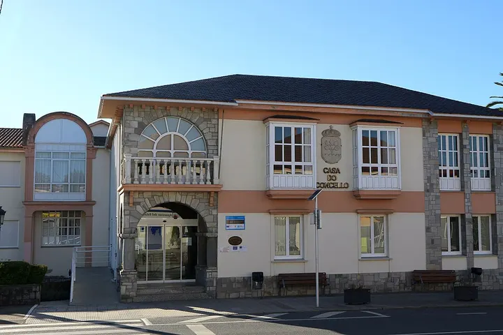 En primer plano, un edificio con una fachada de piedra y ventanas blancas