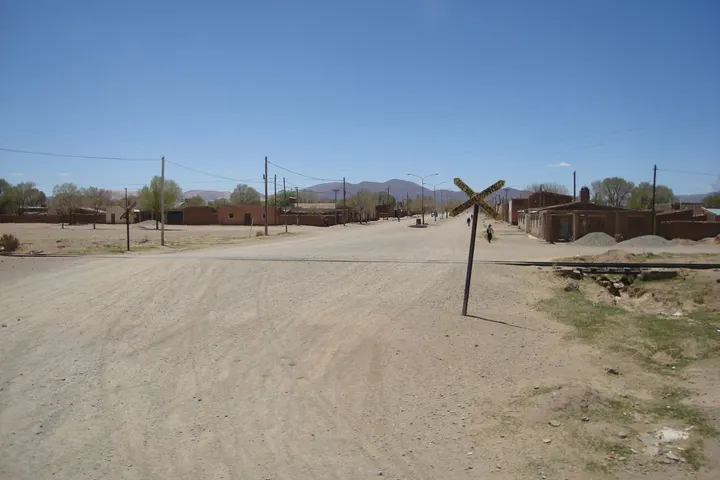 En primer plano, una señal de tráfico en forma de X, con una superficie de tierra arenosa