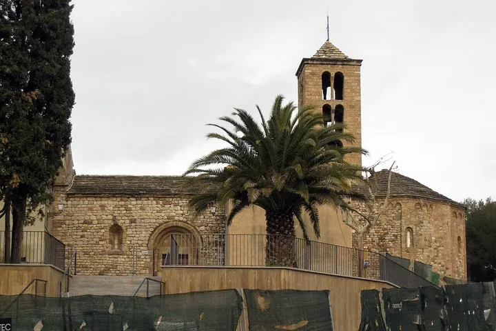 En primer plano, una iglesia de piedra con una torre y un palmero