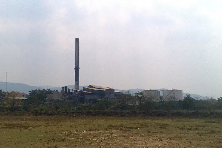En primer plano, una fábrica de cemento con una chimenea alta