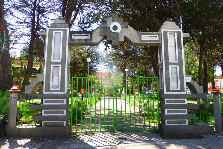 En primer plano, una puerta de un parque con un arco de piedra y un jardín con flores