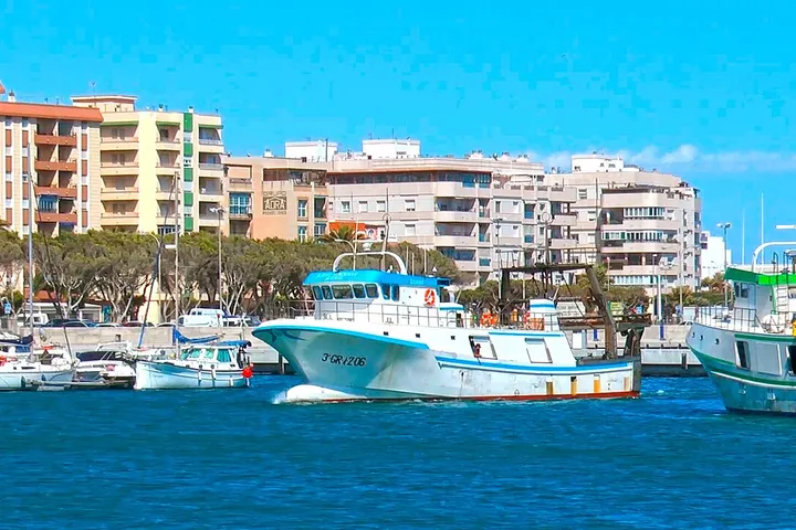 En primer plano, un barco blanco con el número 301215, en un puerto con edificios de varios pisos detrás