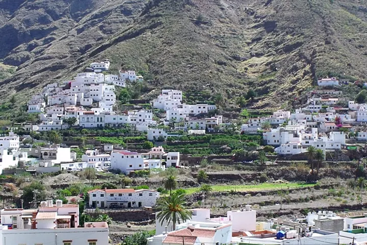 En primer plano, se aprecia un edificio blanco con tejado rojo, rodeado de palmeras y árboles
