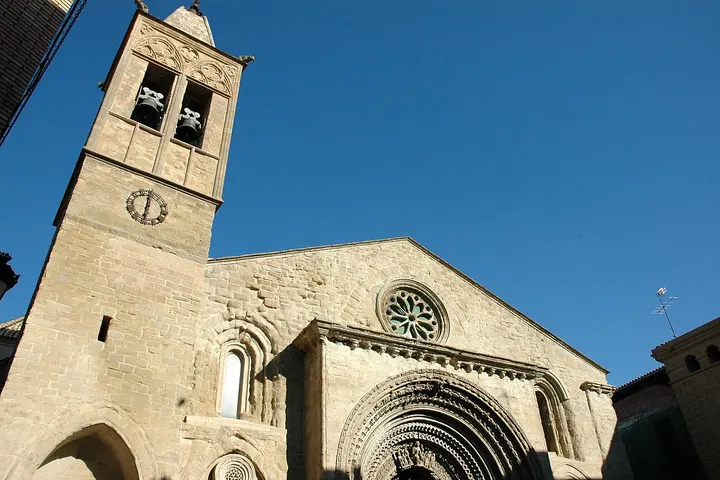 En primer plano, una iglesia con un campanario y una entrada con arco