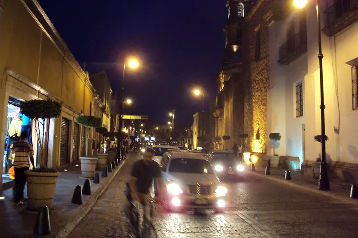 En primer plano, un hombre camina por la calle, mientras un coche pasa por delante de él