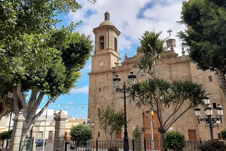 En primer plano, una iglesia de piedra con un campanario y una torre, rodeada de árboles y farolas
