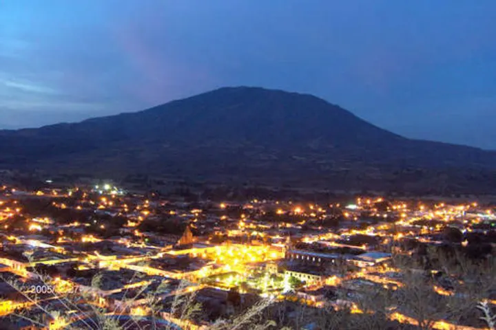 En primer plano, una gran montaña se eleva sobre una ciudad iluminada