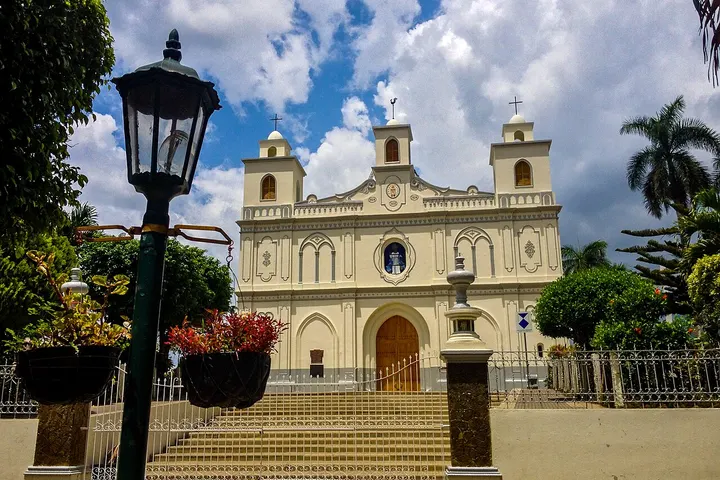 En primer plano, una iglesia blanca con dos torres, una escalera de piedra y un farol de hierro