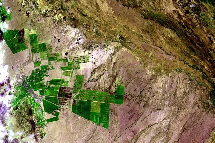 En primer plano, se ven grandes extensiones de terreno cultivado