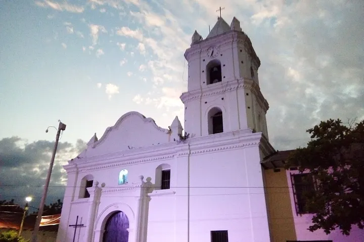 La iglesia de una ciudad, con su torre y puerta principal, bajo un cielo con nubes