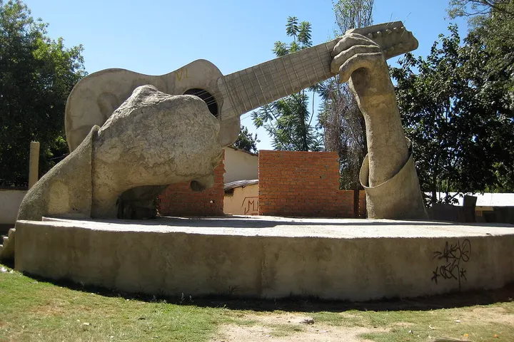 En primer plano, una estatua de un hombre tocando una guitarra