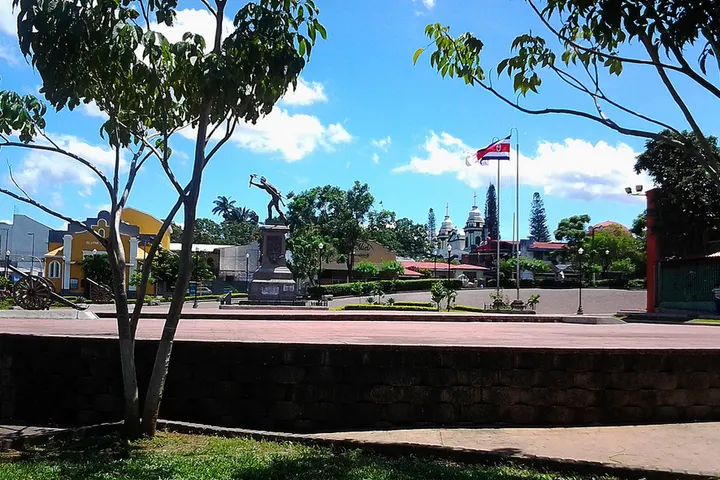 En primer plano, un parque con un monumento de un hombre que parece correr