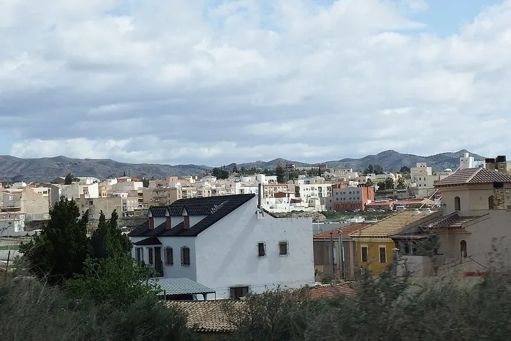 En primer plano, una casa blanca con tejado negro y chimenea