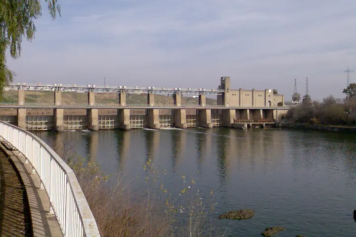 En primer plano, un puente de hormigón sobre un río, con una estructura de madera en su parte inferior