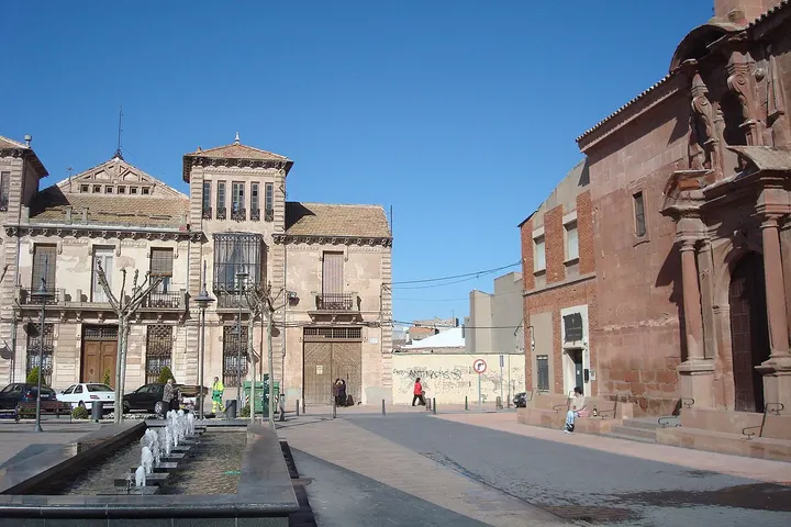 En primer plano, una fuente de agua corriente fluye por un canal en el centro de la calle