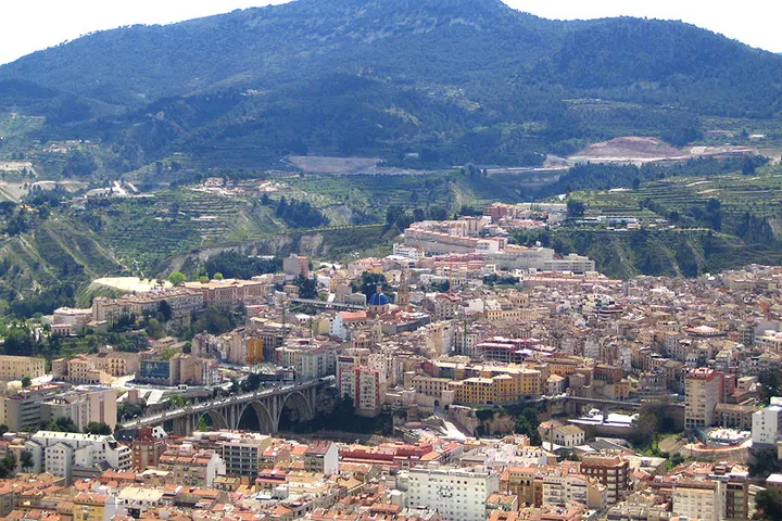 En primer plano se ve una gran puente de arco que cruza un profundo valle rodeado de montañas