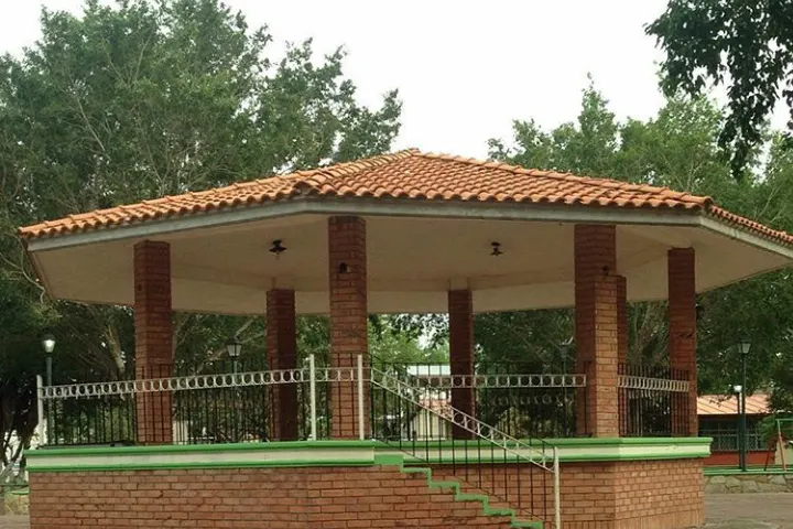 En primer plano, un kiosco de estilo mexicano con techo de tejas y columnas de ladrillo