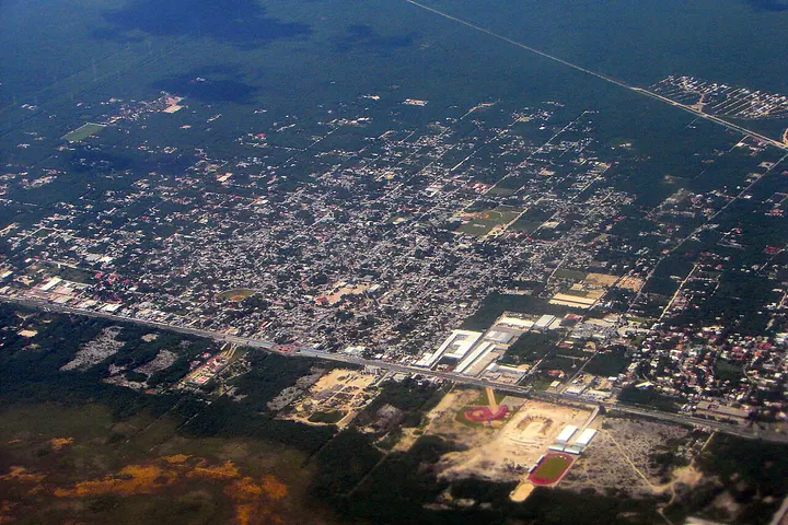 En primer plano, un estadio de fútbol con césped verde y una pista de atletismo rodeada de una cerca