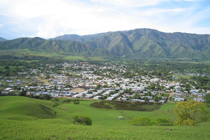 En primer plano se ve una granja con un campo de pasto verde y un pequeño edificio blanco