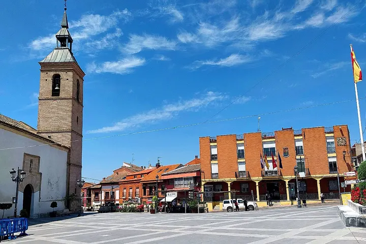 En primer plano, un edificio de ladrillo rojo con balcones y una torre de iglesia con campanario