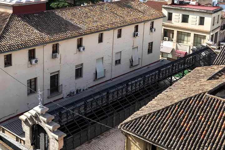 En primer plano, un edificio con tejado de tejas y una torre con una cruz