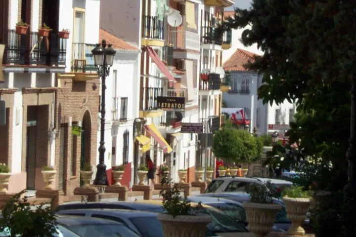 En primer plano, se ven coches aparcados en la calle, con edificios de arquitectura tradicional detrás
