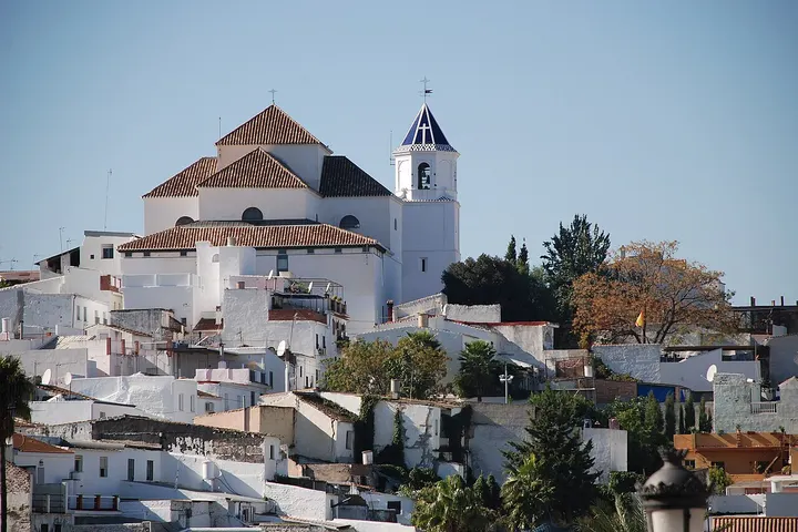 En primer plano, se ve una iglesia blanca con un campanario azul