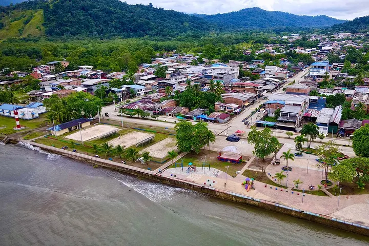 En primer plano, una playa con un parque con juegos infantiles
