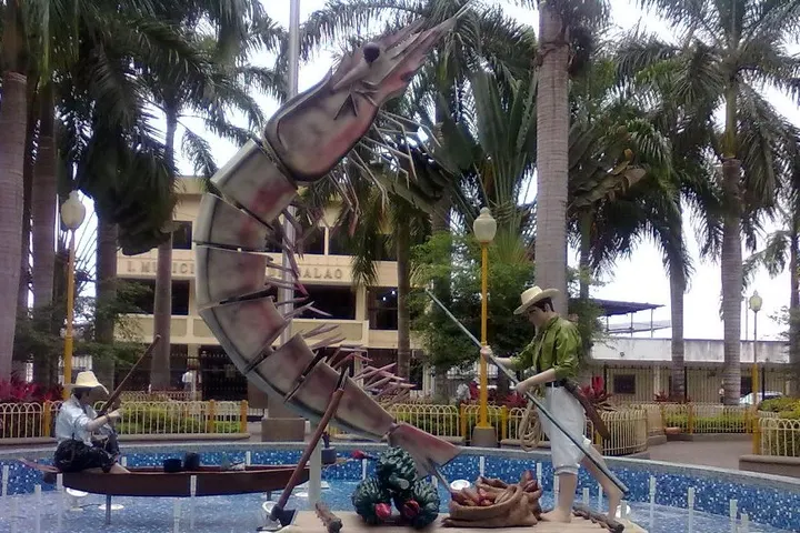 En primer plano, un monumento de un camarón gigante y dos pescadores