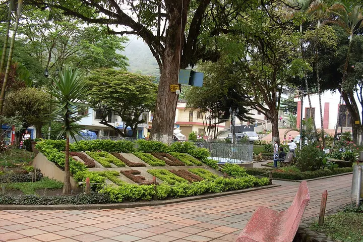 En primer plano, una plaza con un jardín de plantas y árboles