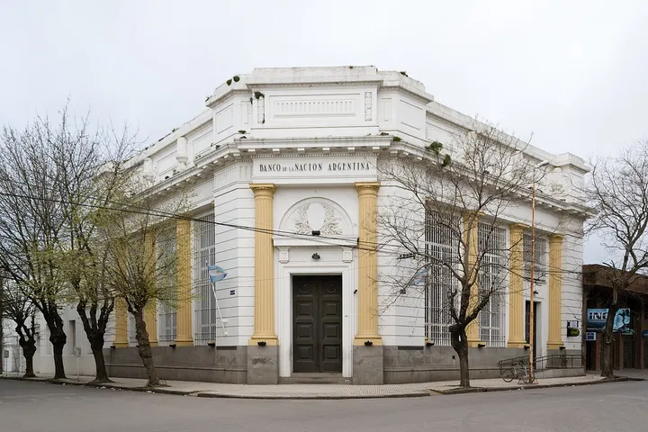 En primer plano, se ve un edificio blanco con columnas amarillas