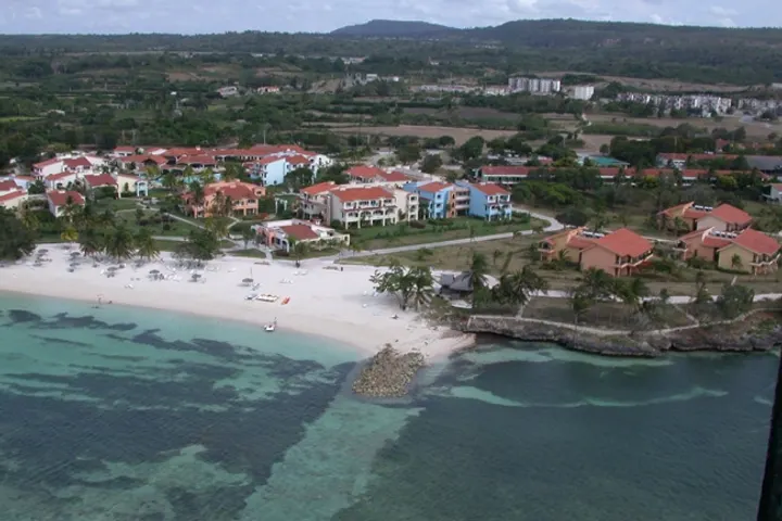 En primer plano, una playa con una zona de arena blanca y aguas cristalinas