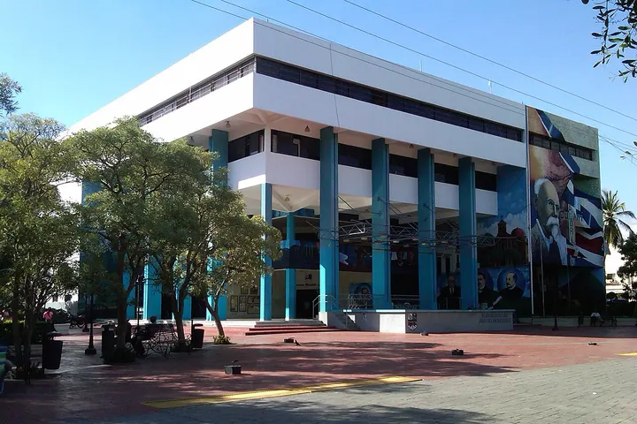 En primer plano, un edificio con columnas azules y una gran pintura mural en su fachada