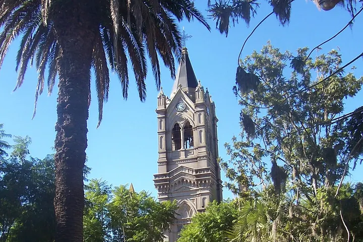 En primer plano, una torre de iglesia con un campanario y una cruz