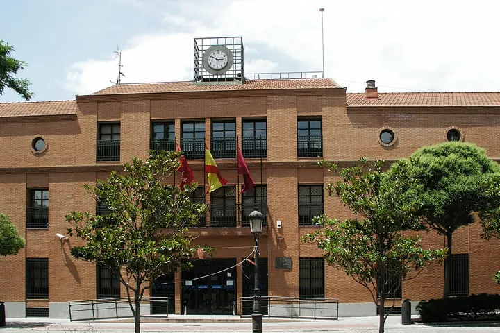 Un edificio de ladrillo rojo con un reloj en el techo y banderas de España y de Castilla y León