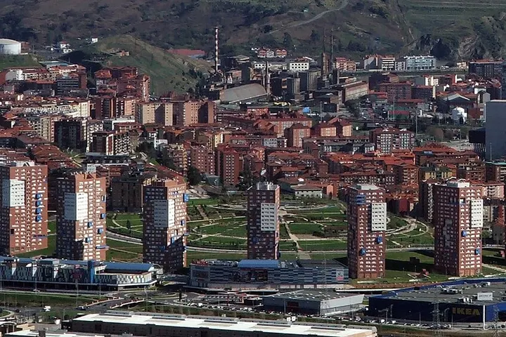 En primer plano, se ven varios edificios altos y un parque con un camino en forma de espiral
