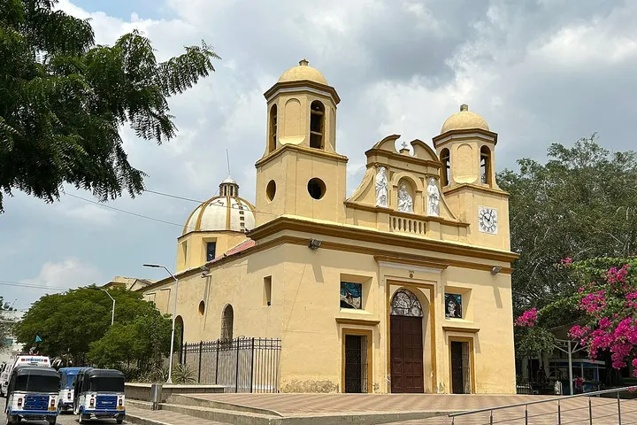 En primer plano, una iglesia de color amarillo con dos torres y una entrada principal