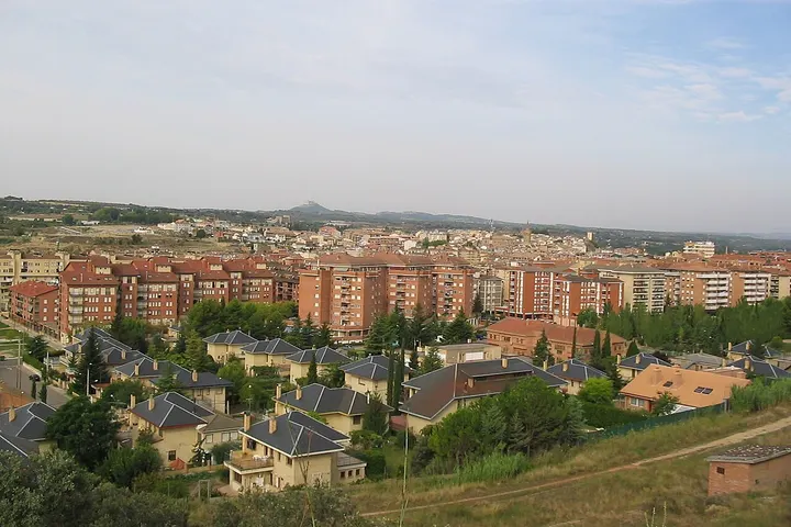 En primer plano, se ven casas con tejados de color gris y amarillo, rodeadas de árboles y arbustos