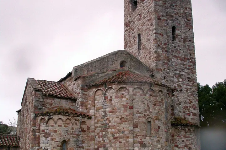 En primer plano, una iglesia de piedra con una torre y un tejado de tejas rojas
