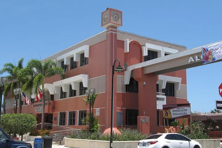Un edificio de color rojo con un reloj en la parte superior, con un coche blanco en primer plano