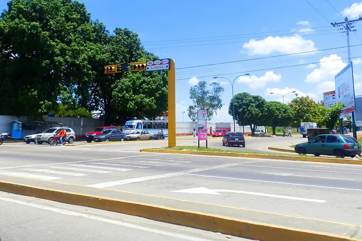 En primer plano, una intersección con un semáforo, un cartel y un poste de señalización