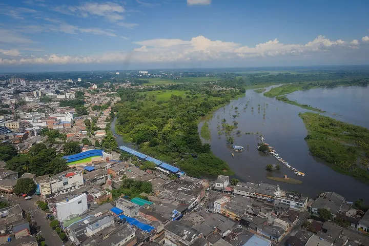 En primer plano, un río rodeado de árboles y una serie de embarcaciones flotando en su superficie