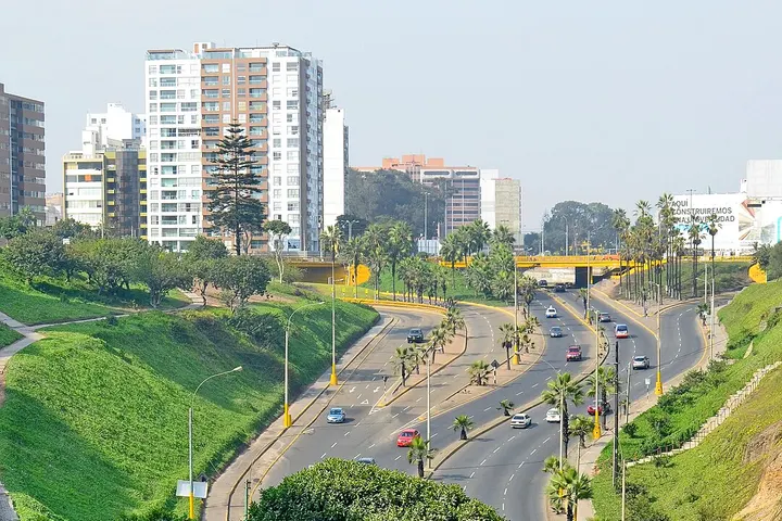En primer plano, se ve un puente de color amarillo sobre una carretera con coches en movimiento