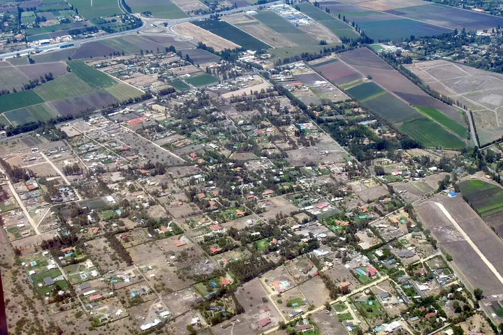 En primer plano, se ve una gran plaza con un parque central rodeado de casas