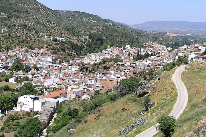 En primer plano, se aprecia una carretera que atraviesa un paisaje rural con casas y montañas