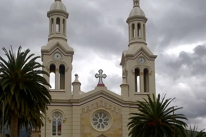 En primer plano, una iglesia con dos torres y una cruz