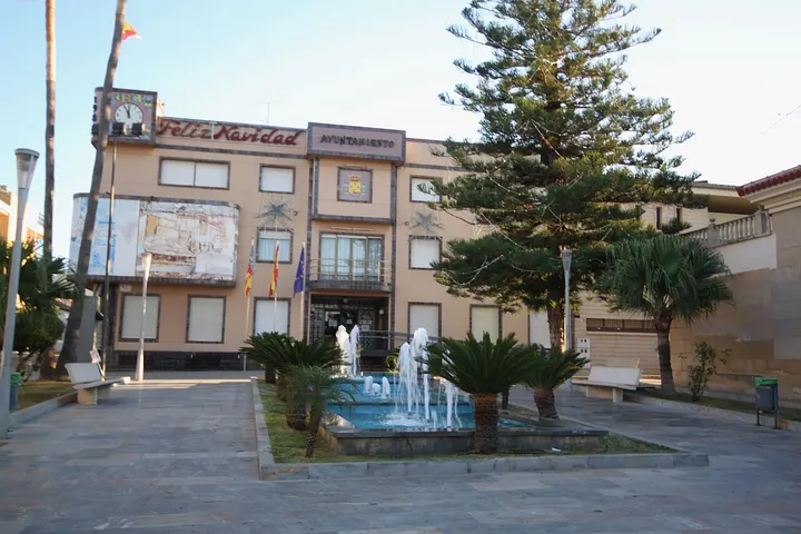 En primer plano, una fuente con estatuas de personas blancas y palmeras