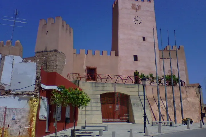 En primer plano, una torre de reloj de color rosa claro con un reloj en su parte superior
