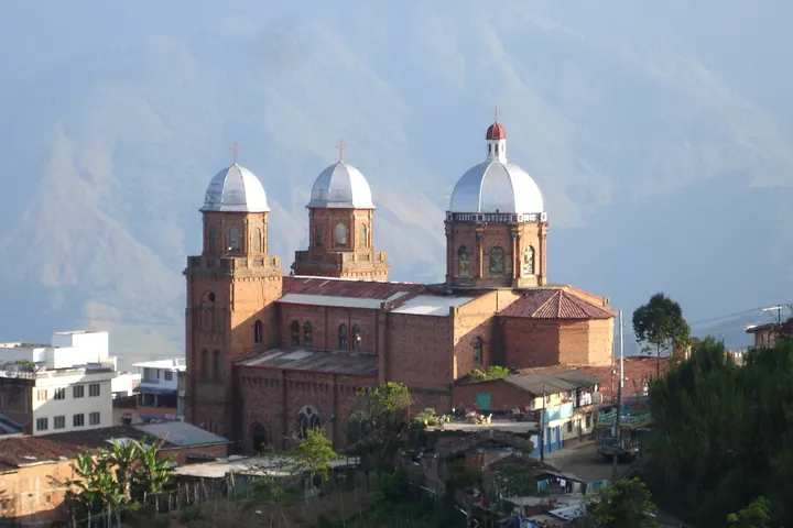 En primer plano, un gran edificio de ladrillo con tres torres de ladrillo y dos cúpulas de metal