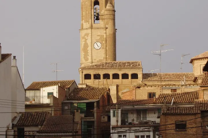 En primer plano, se ve una torre de reloj con un campanario de piedra, con una iglesia detrás